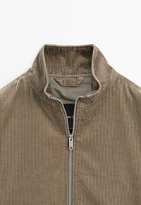 Giacca zip-up in velluto corduroy marrone con colletto alto, strisce verticali testurizzate e chiusura con zip argentata.