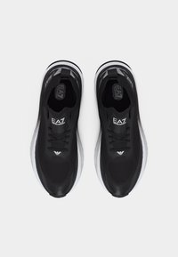 Ζευγάρι μαύρα αθλητικά παπούτσια EA7 Emporio Armani με λευκές σόλες, σε προβολή από πάνω σε ανοιχτό γκρι φόντο.