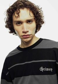 Zwart en grijs gestreepte lange mouwen shirt met een ronde hals en geborduurd logo in het wit op de linkerborst. Zachte stoftextuur.