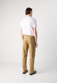 Tan cotton pants with a straight cut, two back pockets, and a flat waistband. Worn with a plain white short-sleeve t-shirt.