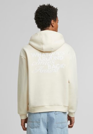 Creme hoodie med et stort hvidt skrift-design på ryggen. Har en hætte med snore og ribbede cuffs ved ærmerne og kanten.