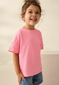 Heldroze katoenen T-shirt met korte mouwen, voorzien van bloemenborduursel op de manchetten, gecombineerd met denim shorts. Eenvoudig ontwerp met ronde hals.