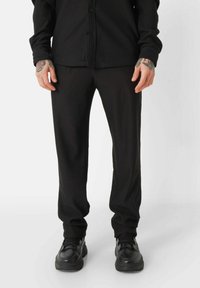 Zwarte geribde stoffen broek met een slim fit, met een gestructureerd oppervlak en elastische boorden. Gecombineerd met zwarte sportschoenen.