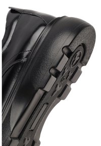 Botte en cuir noir avec une épaisse semelle en caoutchouc noir texturé. Détails cousus le long du corps et design à bout arrondi.