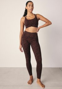 Conjunto de sujetador deportivo y leggins con estampado de leopardo marrón y negro, que presenta un diseño ajustado, textura suave y tirantes finos.