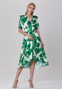 Robe à imprimé tropical vert avec un col en V, des manches courtes, et des détails de boutons, de forme A-line fluide, avec un ourlet asymétrique, fabriquée en tissu léger.