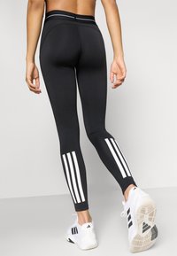 Leggings noirs avec une taille haute, ornés de trois bandes blanches au niveau du mollet. Tissu lisse et extensible pour un ajustement parfait.