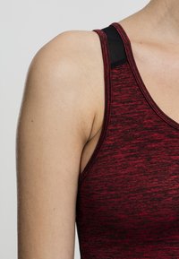 Débardeur de sport rouge et noir, doté d'un tissu texturé, de larges bretelles et d'un panneau épaule noir contrastant.