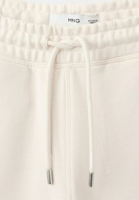 Talie elastică albă cu șnur și capete metalice pe pantaloni din material ușor, cu etichetă vizibilă a mărcii "MNG".