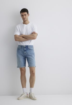 Light blue denim shorts with rolled cuffs, paired with a plain white crewneck t-shirt. Shoes are beige with red accents and white socks.