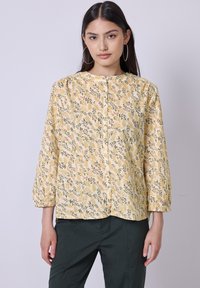 Blouse jaune à manches longues avec motif floral comportant des feuilles et de petits accents roses, avec un col rond.
