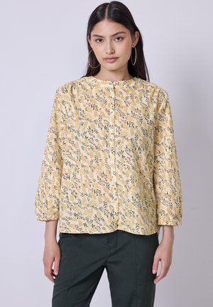 Blusa gialla con bottoni, caratterizzata da un motivo floreale con foglie e piccoli accenti rosa, maniche lunghe e scollatura rotonda.
