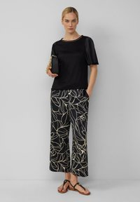 Czarny satynowy top z krótkimi rękawami, w zestawieniu z szerokimi czarnymi spodniami z kremowym wzorem liści. Czarna torebka na łańcuszku, płaskie sandały.
