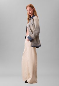 Spijkerjack met een lichtgrijze vervaging, donkerblauwe kraag en twee zakken aan de voorkant, gecombineerd met wijde crèmekleurige broekspijpen en zwart schoeisel.