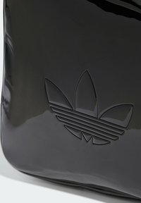 Black glossy bag featuring an embossed Adidas logo with three petals and horizontal stripes. Smooth texture with clean, modern lines.