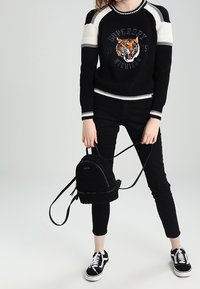 Pull noir côtelé avec accents blancs et motif tigre, associé à un jean skinny noir et un petit sac à dos noir duveteux. Baskets noires.