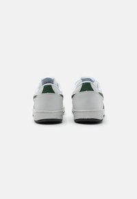 White sneakers with green accents, leather material, low-top design, rounded toe, rear pull-tabs, and contrasting black rubber sole.