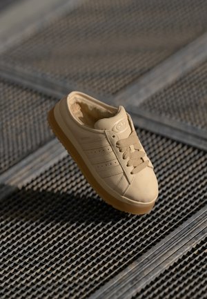 Sneaker beige con tomaia in pelle liscia, linguetta testurizzata, design a tre strisce e suola in gomma naturale, con lacci e dettagli tonali.