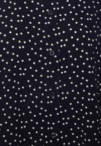 Navy button-up shirt with white polka dots, featuring black buttons and a soft, textured fabric.