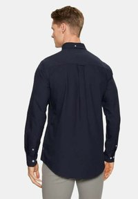 Camicetta a maniche lunghe di colore blu navy in un tessuto morbido con orlo curvo. Presenta dettagli per una vestibilità adeguata, tra cui polsini con bottone e piega sul retro.