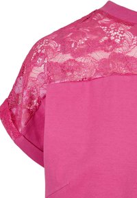 Roze jurk met korte mouwen en een kanten overlay, naadloos ontwerp en een zachte textuur. Het kant heeft bloemmotieven voor extra detail.