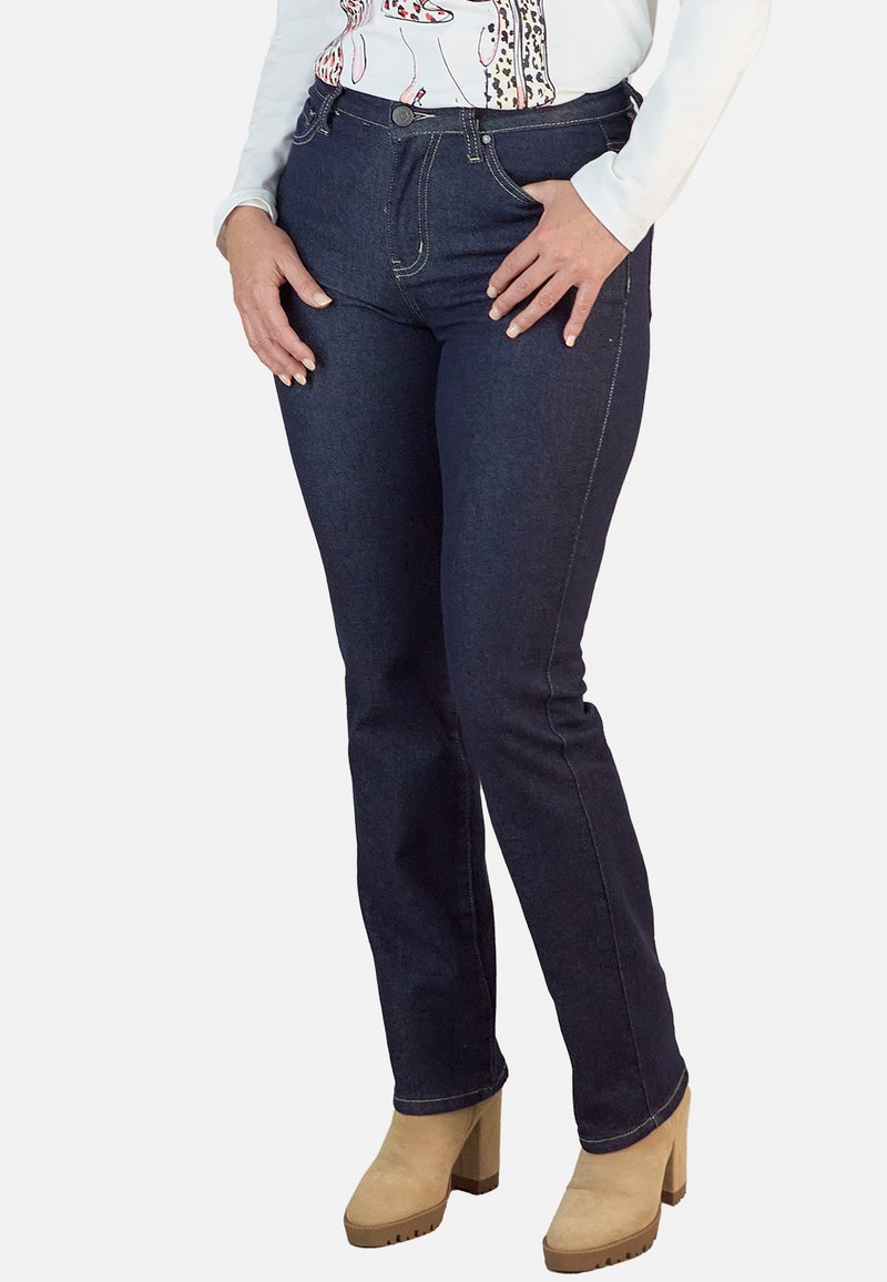 Vaqueros de denim azul oscuro con cintura alta, que presentan un clásico diseño de cinco bolsillos y costuras amarillas contrastantes, combinados con botas de plataforma marrones.