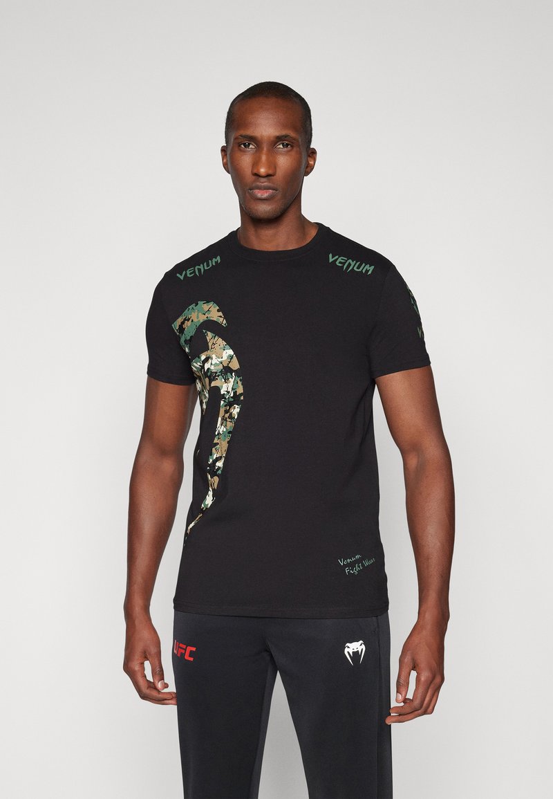 T-shirt en coton noir avec un logo "Venum" vert et un design camouflage sur le côté gauche ; manches courtes, col rond.