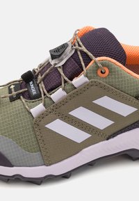Outdoor shoe featuring a textured green upper, grey accents, reflective details, and a quick-lacing system with orange lining and black outsole.