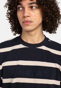 Mørkeblå og cremefarvet stribet t-shirt med rund hals, der har et tekstureret "element" logo broderet på brystet. Blød stoftekstur.