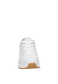 Zapatilla deportiva blanca con parte superior de material sintético liso, diseño de cordones, detalles perforados para transpirabilidad y suela de goma con agarre texturizado.