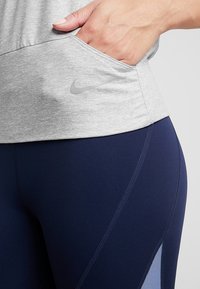 Gray athletic top with a side pocket and a subtle logo, paired with dark blue leggings featuring a light blue panel and stitching details.