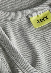 Tessuto grigio a righe con scollo a V, caratterizzato da un'etichetta gialla brillante con "JJXX" stampato in nero. Texture liscia e motivo sottile.