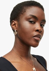 Gold and silver hoop earrings with linked design, against a dark background featuring a smooth neck and short textured hair.
