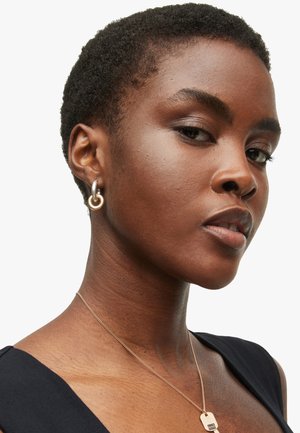 Gold and silver hoop earrings with linked design, against a dark background featuring a smooth neck and short textured hair.
