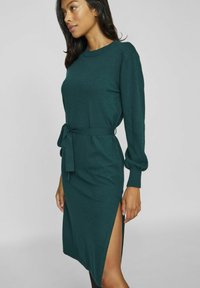 Rochie tricotată turcoaz cu manșete lungi, slit lateral și talie ajustabilă. Prezintă un guler rotund și o textură moale.