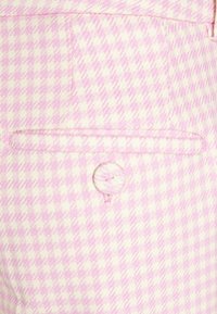 Rosa og hvidt houndstooth-mønster stof med en lille lomme og en matchende knap. Struktureret materiale med en let vævning.