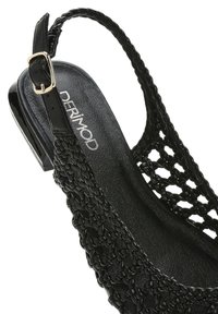 Sandalo slingback nero con dettagli intrecciati, una soletta nera testurizzata e un tacco lucido. Dettaglio a fibbia sulla cinghia regolabile.