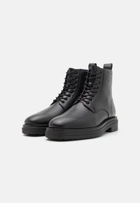 Bottines noires en cuir avec une finition lisse, bout rond et design à lacets. Comprend une semelle en caoutchouc noire épaisse et une languette à l'arrière.