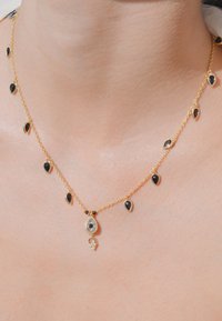 Collier en chaîne dorée avec des pierres noires en forme de goutte, présentant un élément décoratif central et de plus petits accents, créant un design délicat.