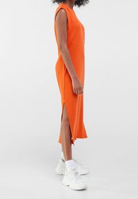 Robe sans manches orange avec des fentes sur les côtés, fabriquée en tissu côtelé. Assortie à des baskets blanches à semelles épaisses et des chaussettes blanches pour le contraste.