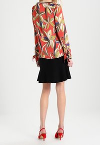 Röd blus med färgglada bladmönster och långa ärmar, i kombination med en svart utsvängd kjol och röda högklackade skor.