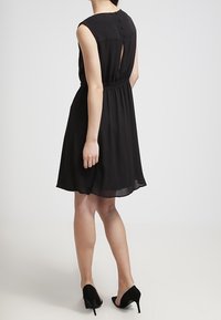 Abito in chiffon nero con vita aderente, design senza maniche e dettaglio a chiave sulla schiena. Accentuato da una trama liscia e fluida.