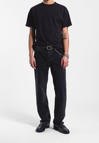 Camiseta de algodón negra, de corte holgado, combinada con jeans de mezclilla negros. Lleva un cinturón de cadena y mocasines negros. Colores sólidos y claros en todo el conjunto.