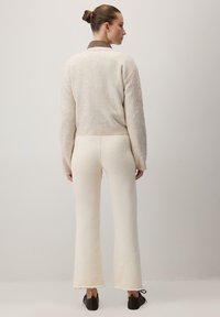 Pulover bej tricotat, cu un design scurt și un model de tricot cu cabluri, asociat cu pantaloni albaștri cu o margine evazată și o textură moale.