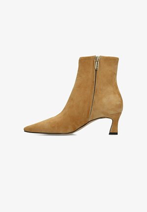 Bottine en daim beige avec bout pointu, talon kitten de hauteur moyenne et fermeture éclair latérale.