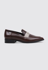 Mocasines de cuero marrón con punta afilada y un acento de tira en contraste de color marrón claro. Suela plana negra, textura suave y diseño minimalista.
