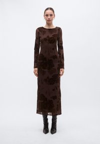 Pika varrukaga, keha järgnev pruun kleit läbipaistvast kangast, millel on lilleline samettrüüm, ümmarguse kaelusega ja pahkluu pikkune. Sobitatud mustade põlviksaabastega.