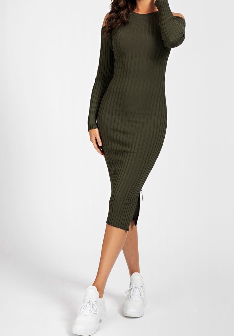 Robe côtelée vert olive avec des manches longues, design dénudé d'épaules, coupe au genou et fentes sur les côtés ; associée à des baskets blanches.
