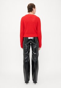 Červený pletený svetr s kulatým výstřihem, kombinovaný s kalhotami z černé lakované kůže s vysokým pasem. Tento outfit je přiléhavý a elegantní.