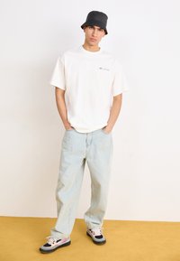 Hvid bomulds t-shirt med korte ærmer og et lille farverigt logo, parret med lyseblå, løse denim jeans og en sort bucket hat.